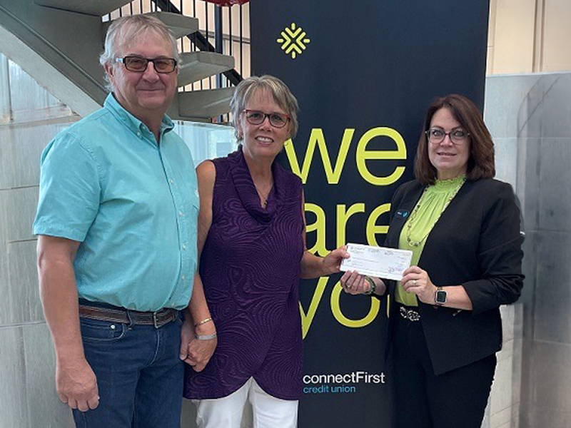 Donate_2 Three people pose indoors in front of a connectFirst Credit Union banner, holding a donation cheque during a presentation photo.