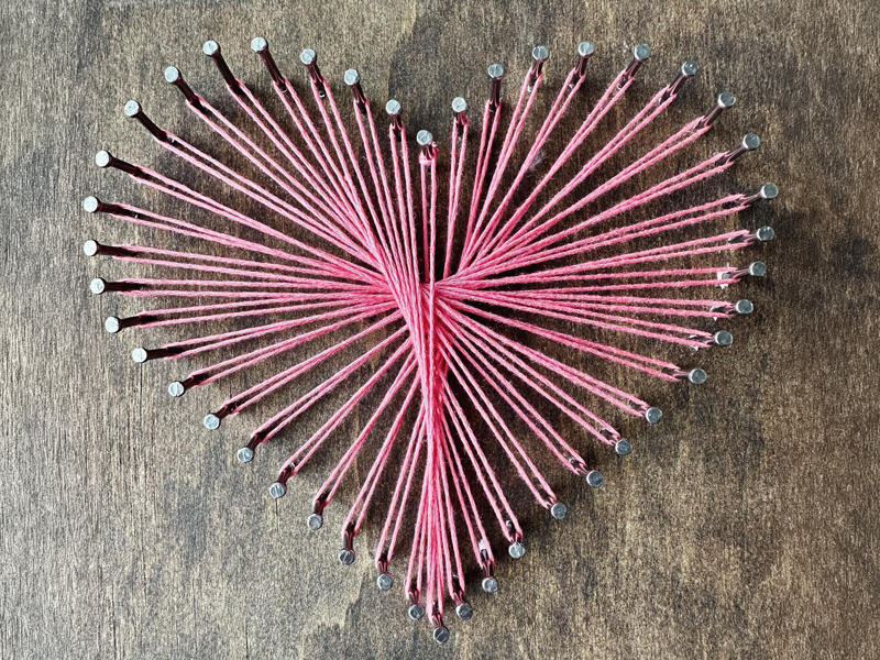 Make-&-Mingle_2 Heart-shaped string art made with pink thread wrapped around nails on a wooden board, a simple “Make & Mingle” craft for connection and creativity.
