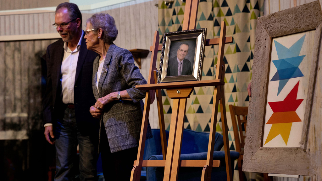 Ron-and-Betty-Hilton-Family At a HopeBridges (hopebridges.ca) commemorative event, guests stand beside an easel displaying a framed portrait and colourful artwork, honoring the Ron and Betty Hilton Family.