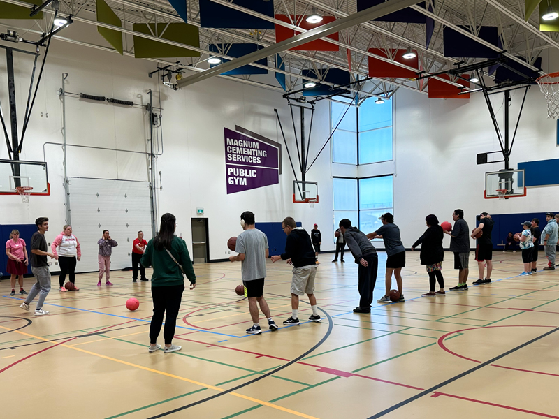 Way2Move_2 Adults line up in a community gym with basketball hoops, holding and tossing red balls during a HopeBridges Way2 Move adaptive sports session focused on mobility, coordination, and active living.