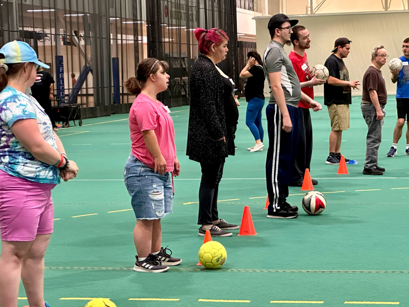 Way2Move_3 Adults stand in a line on an indoor gym court with cones and soccer balls during a HopeBridges (hopebridges.ca) Way2 Move adaptive sports session, building mobility and coordination through inclusive active play.